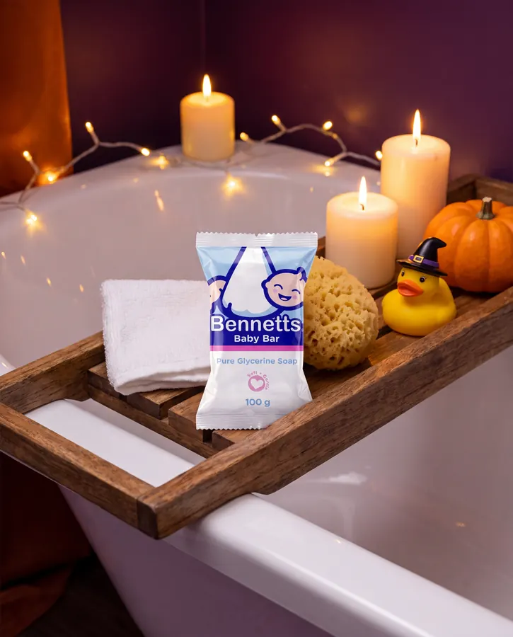 A Bennetts Baby Bar on a wooden bath caddy with a sponge, a witch-hat rubber duck, candles and a pumpkin