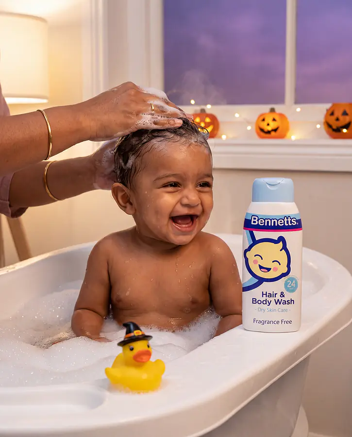 A laughing baby in a bubble bath while his mom lathers his hair, with Bennetts Hair & Body Wash on the tub rim and jack-o’-lanterns on the windowsill