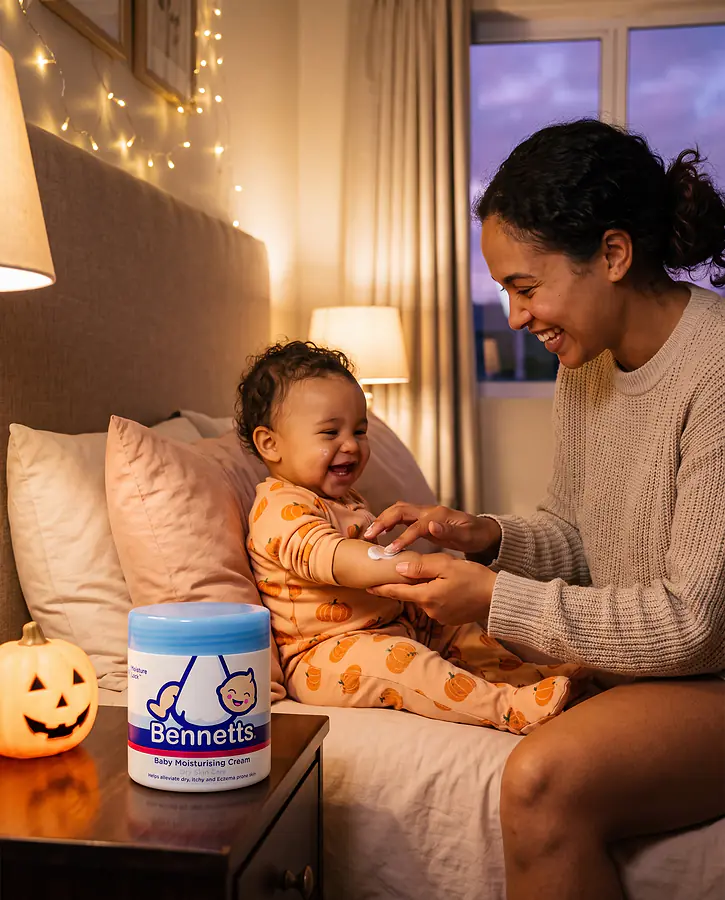 A mom smoothing Bennetts Moisturising Cream onto her giggling baby in pumpkin pyjamas at bedtime, with the tub on the nightstand