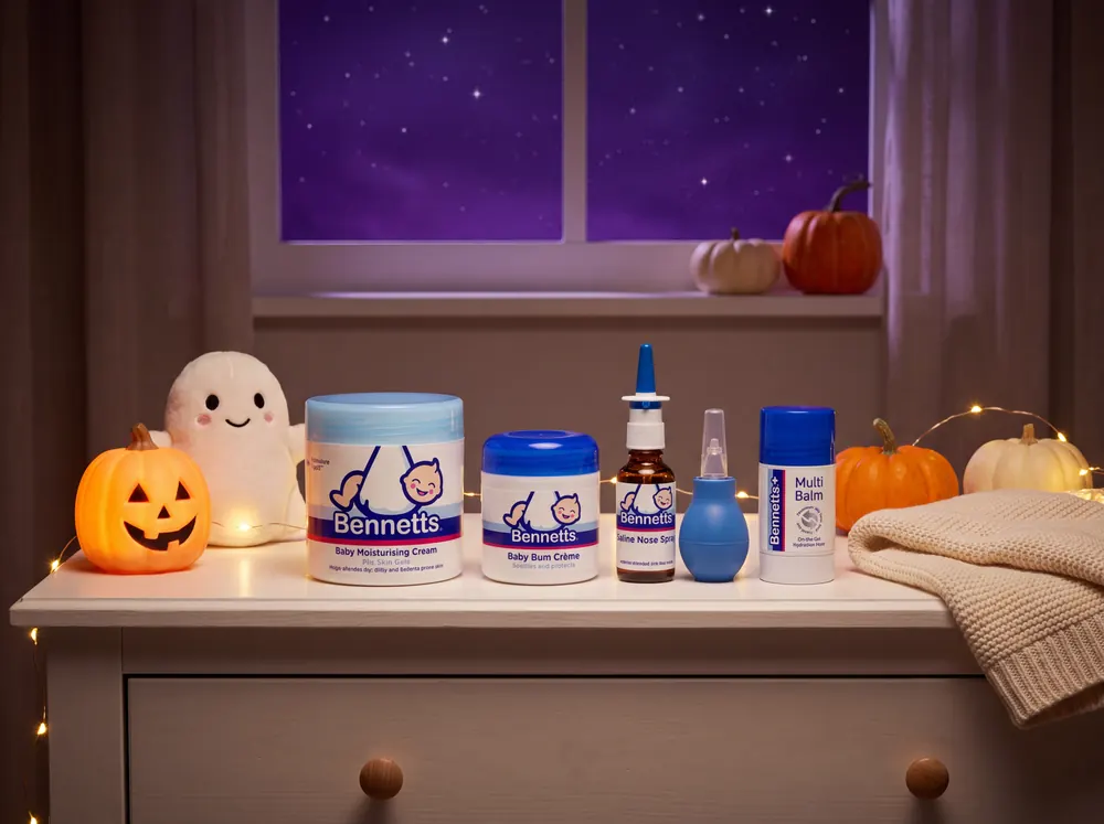 Bennetts Moisturising Cream, Baby Bum Crème, Saline Nose Spray, a nasal aspirator and Multi Balm on a dresser with a ghost plush and a pumpkin lamp